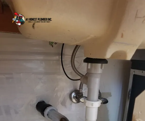 Underside view of a kitchen sink showing the garbage disposal unit and PVC drainage pipe connections.